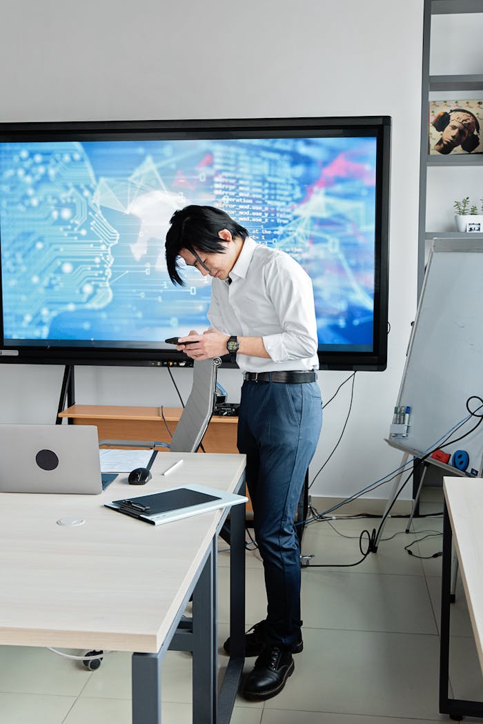 A man standing in an office checks his smartphone with a digital screen displaying AI graphics.